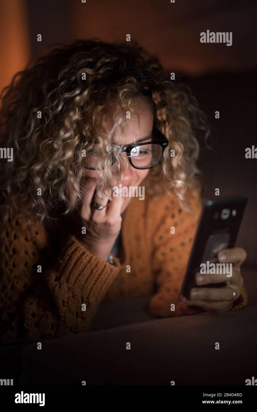 Junge Frau zu Hause lächelt und nutzt das Handy nachts auf dem Sofa - Menschen mit moderner Technologie, um die Internet-Webmedien zu verbinden und zu durchsuchen Stockfoto
