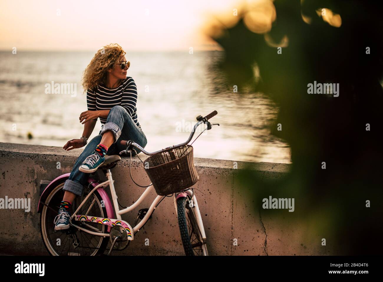 Erwachsene kaukasische Frau, die Outdoor-Freizeitaktivität genießen nach einer Fahrt mit einem Vintage-Fahrrad entspannen und an einer Wand sitzen, die auf das Meer blickt - gesunde aktive Lifestyle-Leute Stockfoto