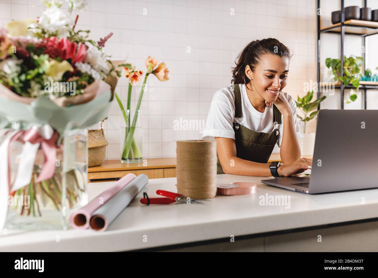 Lächelnder Blumenhändler mit Laptop. Blumenfrau arbeitet an einem Laptop an der Theke. Stockfoto