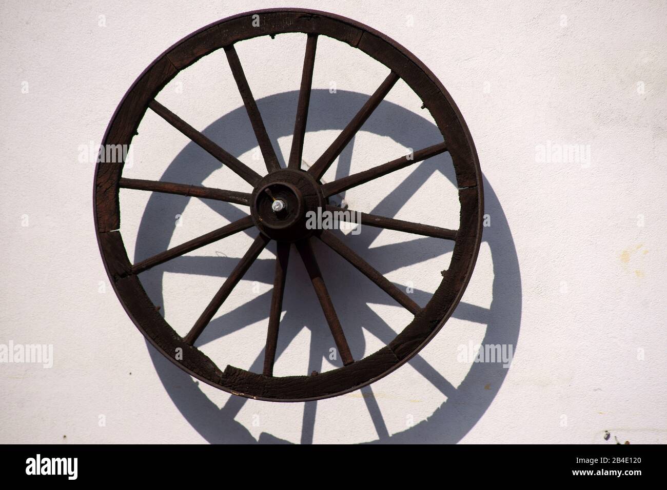 Eine alte, nostalgische Speichenrad eines Trainers oder eines Anhängers an der Wand eines Bauernhaus für dekorative Zwecke hängt. Stockfoto