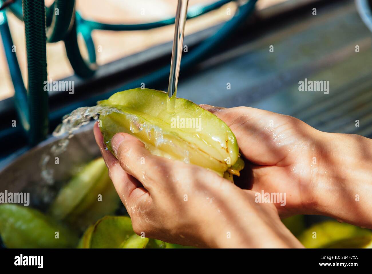 Nahaufnahme der Frau, die frische organische Sternfrucht (Averrhoa carambola), alias Carambola, waschen, unter fließendem Wasser spülen und mit den Fingern scheuern Stockfoto