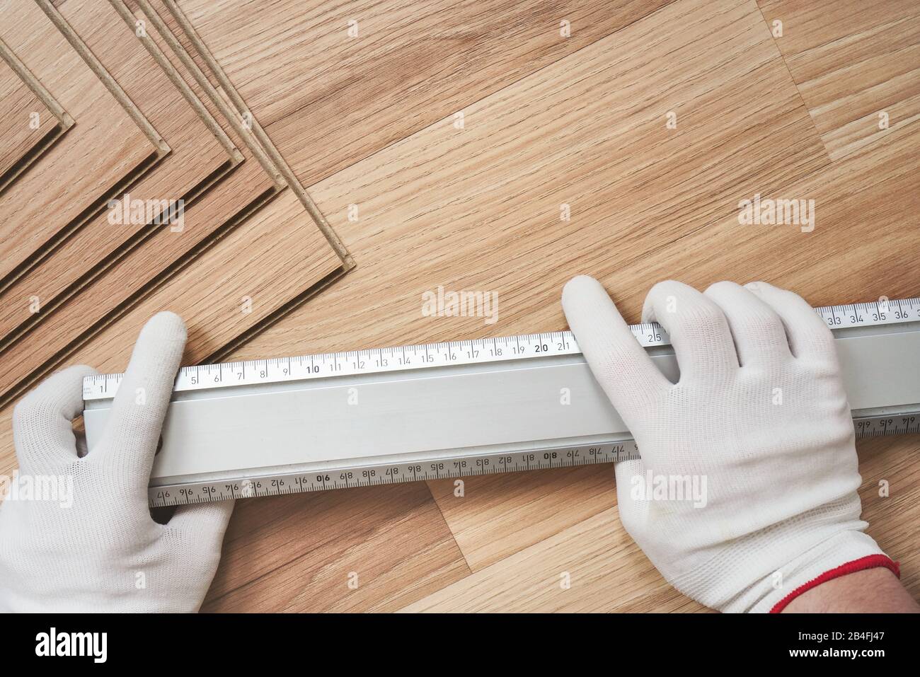 Laminierter Boden, Detail auf den Händen des Menschen mit weißen Handschuhen, die das Metalllineal über Holzfliesen halten, Sichtform oben. Stockfoto