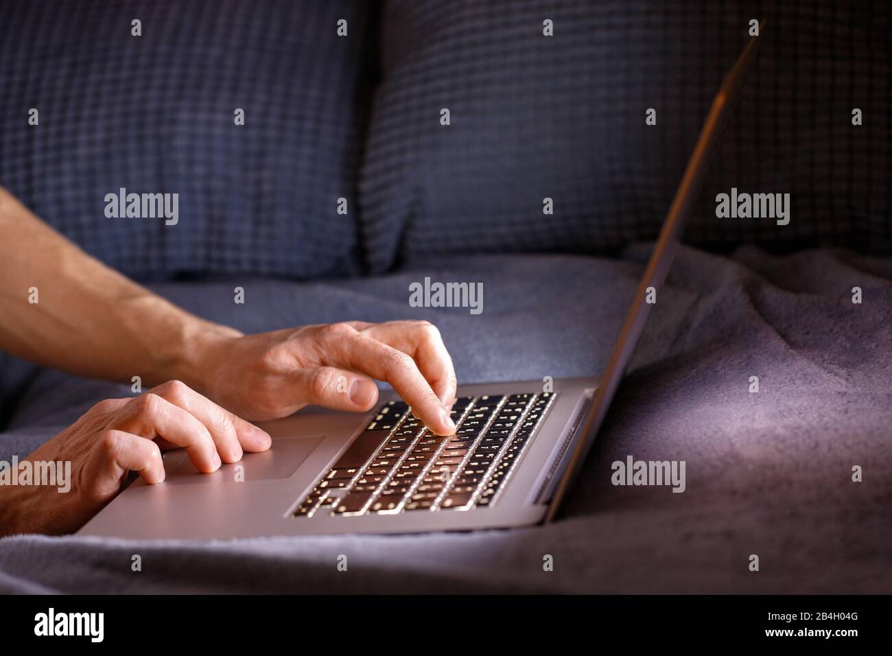 Nahaufnahme von Mann Hände Tippen auf der Laptop-Tastatur nachts drinnen, Kopierraum. Telearbeit, Heimarbeit, freiberufliches Konzept Stockfoto