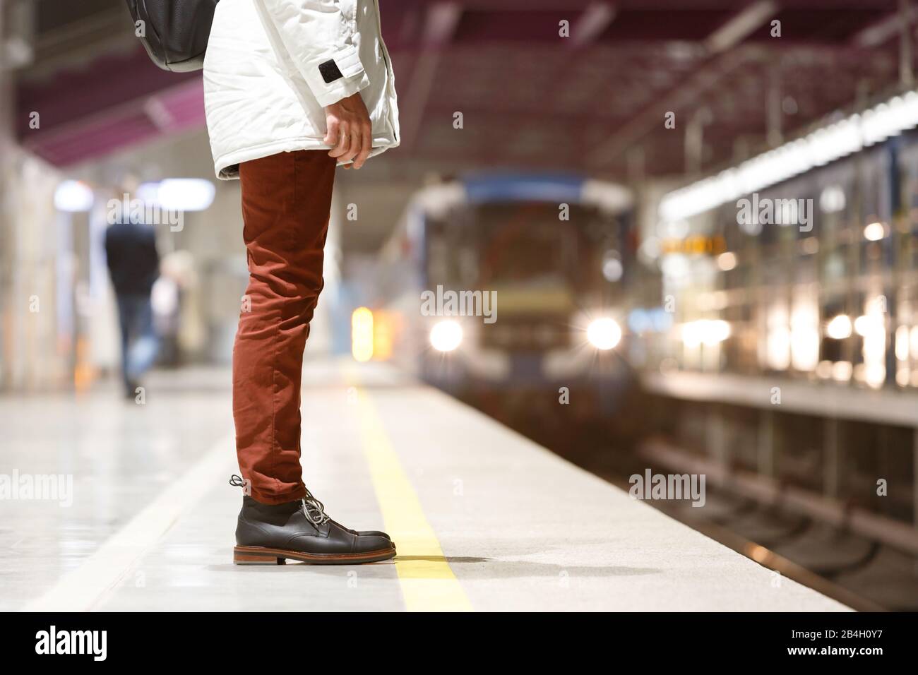Nahaufnahme des Mannes, der am frühen Morgen an der U-Bahn-Station wartet, und geht zur Arbeit, mit weißem Parka, roter Jeans, braunen Lederstiefeln und leerem U-Bahn-Pl bekleidet Stockfoto