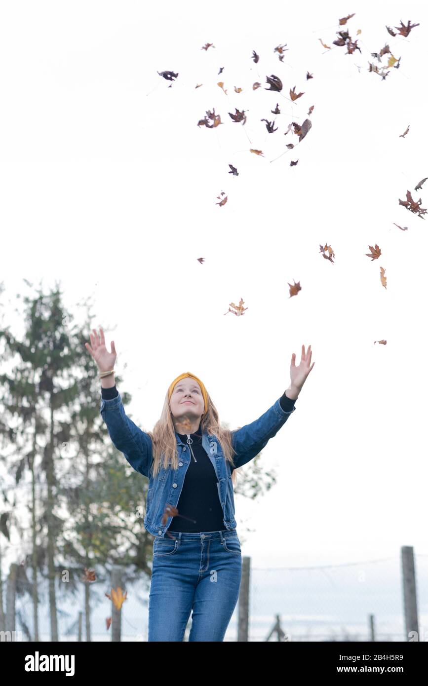 Ein zwölf Jahre altes Mädchen wirft Blätter in die Luft und genießt den Sturz Stockfoto