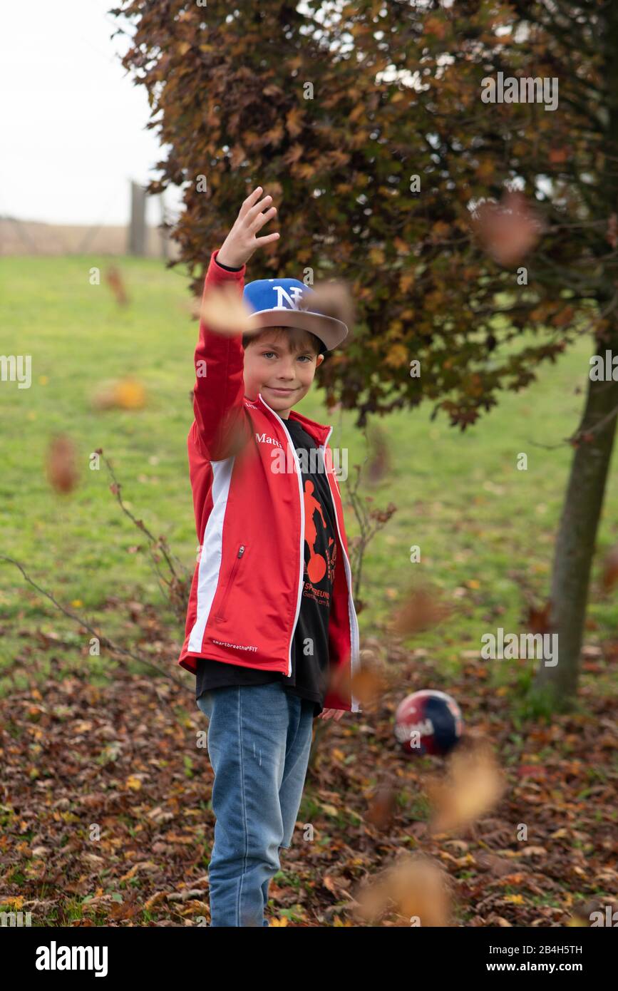 Ein achtjähriger Junge wirft Blätter in die Luft, er freut sich auf den Herbst und das nächste Fußballspiel, im Hintergrund steht sein Fußball vom französischen Verein Paris Saint Germain, Stockfoto