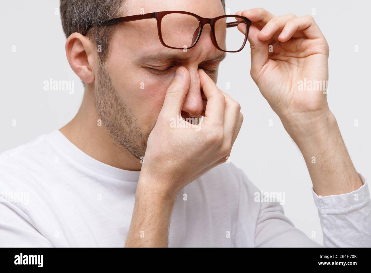 Nahaufnahme des Menschen in Brillen, die seine Augen und Nasenbrücke reiben, fühlt sich müde an, nachdem er an einem Laptop gearbeitet hat, isoliert auf weißem Hintergrund. Überarbeit, Stockfoto