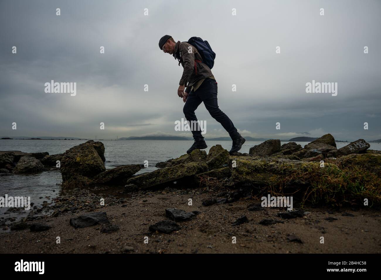 Wanderer gehen über moosige schlammige Steine von der Struktur am Strand an der Bucht Stockfoto