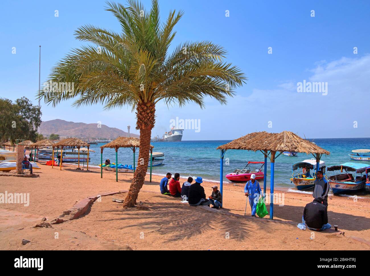 Einheimische am Stadtstrand mit Ausflugsbooten und Blick auf den Akaba Akaba Hafen, Golf von Akaba, Rotes Meer, Jordanien Stockfoto
