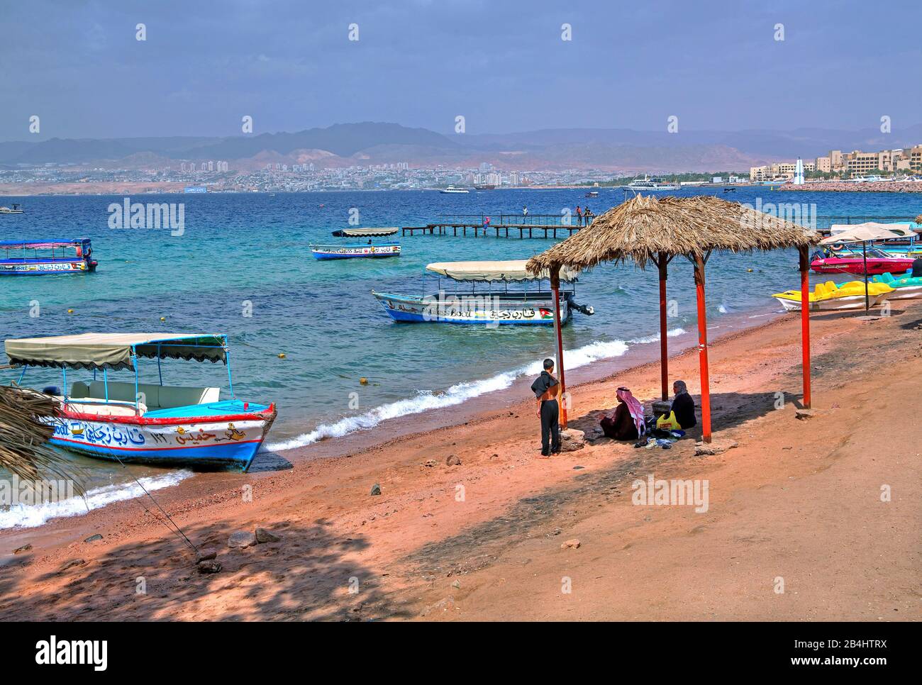 Einheimische am Stadtstrand mit Ausflugsbooten und Blick auf Eilat Akaba Akaba, Golf von Akaba, Rotes Meer, Jordanien Stockfoto