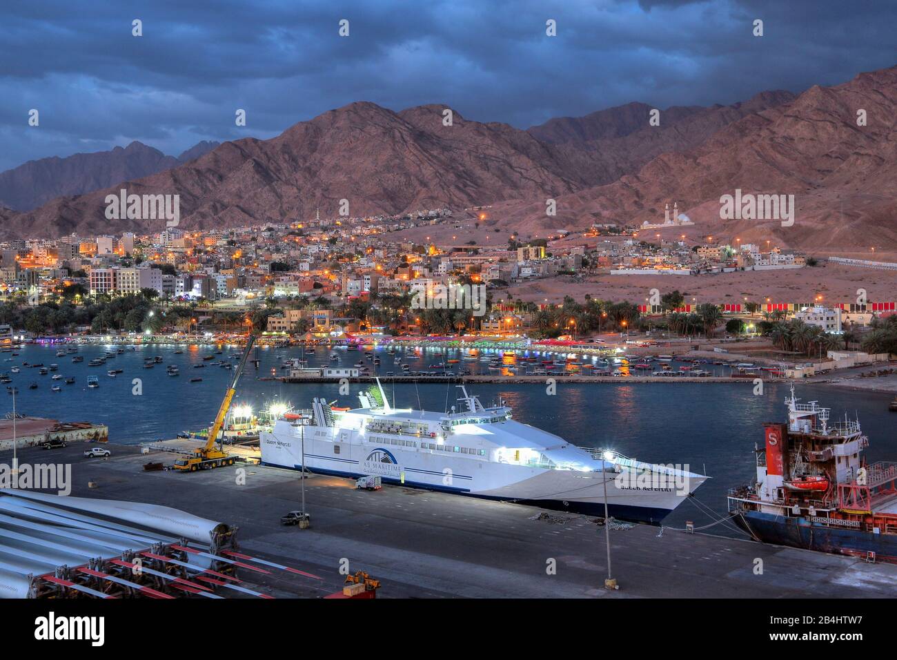 Fähre im Hafen gegen die Stadt mit Wasserfront und Bergen in der Nacht, Akaba Akaba, Golf von Akaba, Rotes Meer, Jordanien Stockfoto