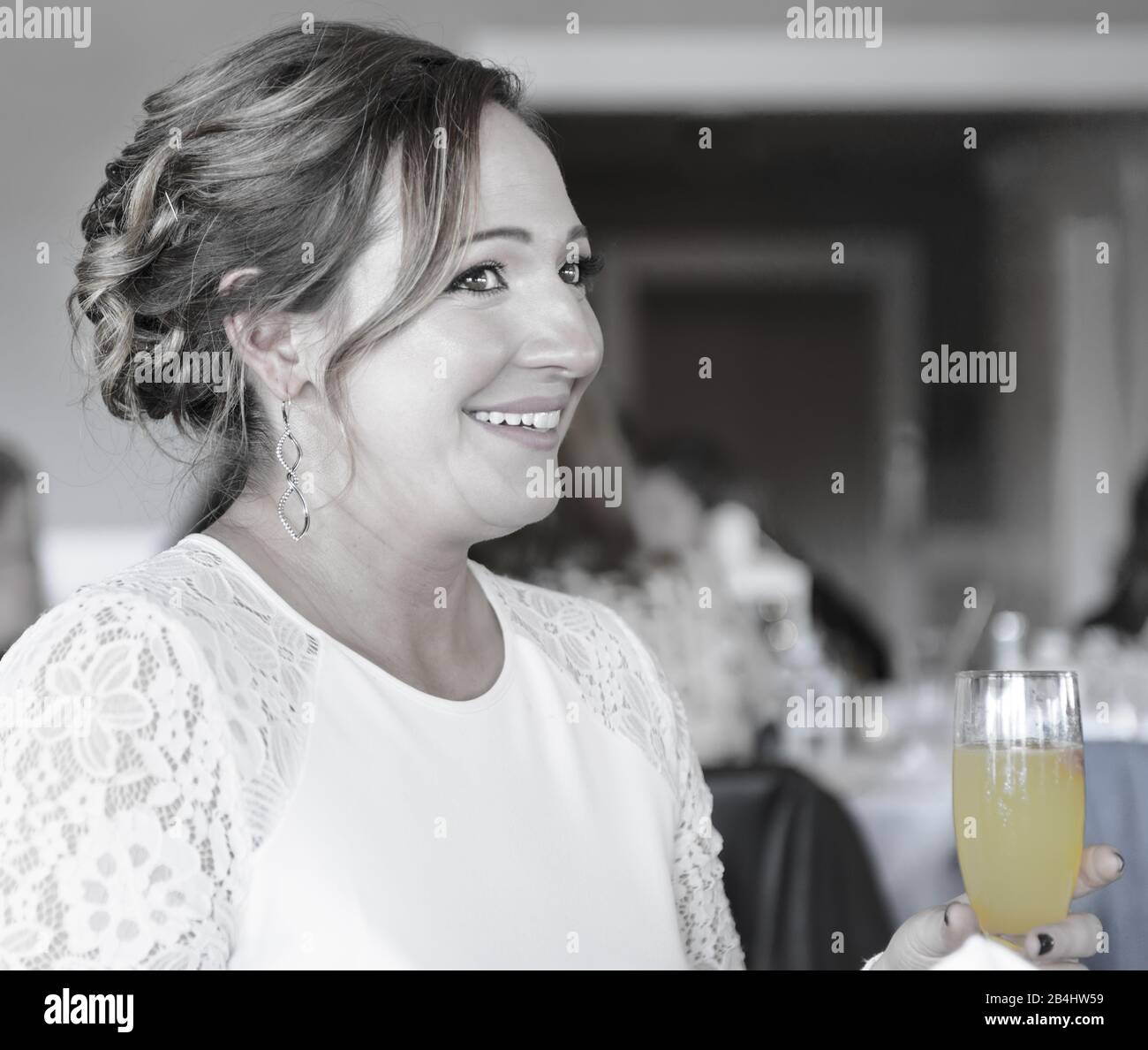 Nahaufnahme einer lächelnden, hübschen jungen Frau, die sich bei einer Veranstaltung in einem weißen Kleid mit einer Mimose bekleidet hat Stockfoto