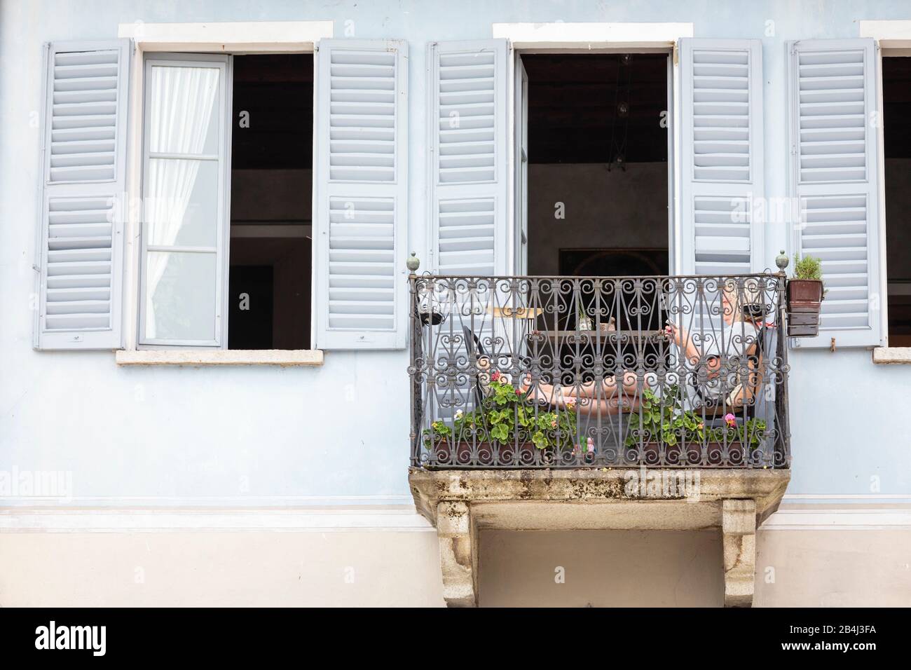 Europa, Italien, Piemont, Cannobio. Eine Frau sitzt auf einem kleinen Balkon und am besten. Stockfoto