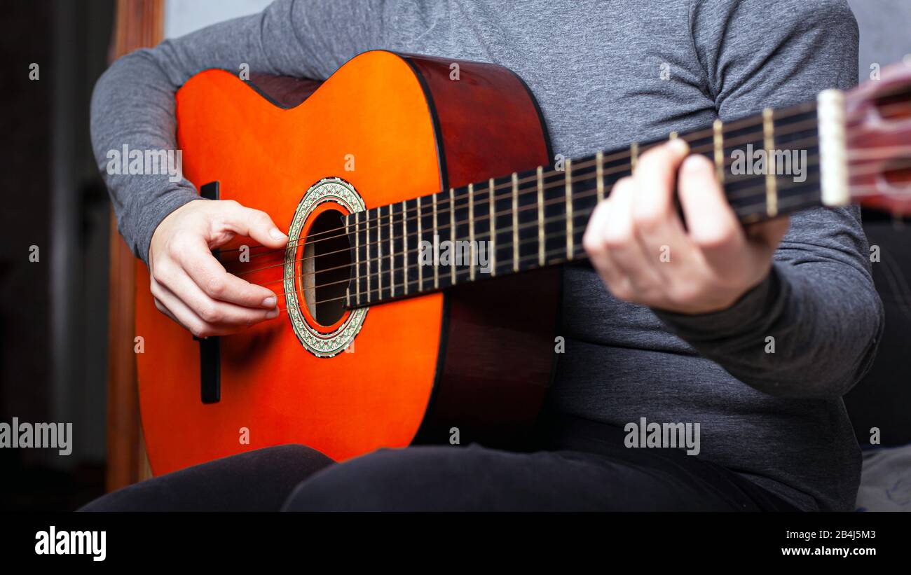 Mädchen, die eine orangefarbene Akustikgitarre spielen, greifen den Akkord auf dem Griffbrett. Musikinstrumentenunterricht Nahaufnahme. Stockfoto