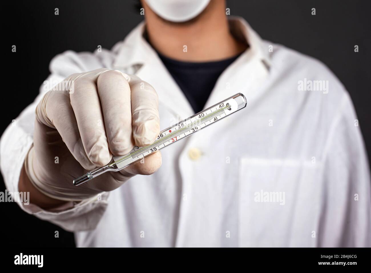 Doktor in einem weißen Mantel in einer Maske und Handschuhe hält ein Thermometer in der Hand. Behandlung auf virale und bakterielle Krankheit prüfen.Körpertemperatur erhöht f Stockfoto