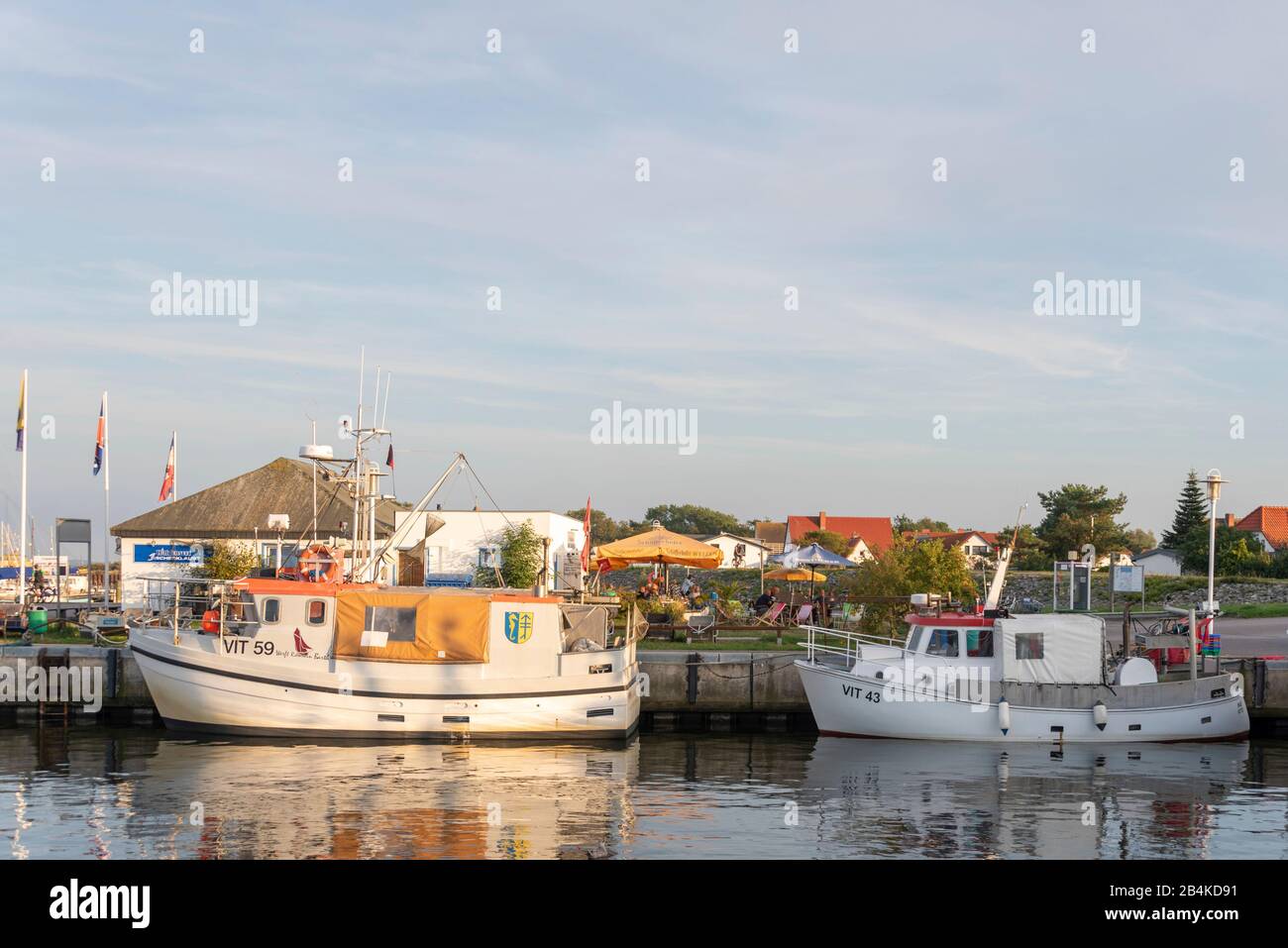 Deutschland, Mecklenburg-Vorpommern, Hiddensee, Boote befinden sich im Hafen von Vitte, dahinter sitzen Touristen auf der Terrasse eines Fisch-Imbisses. Stockfoto