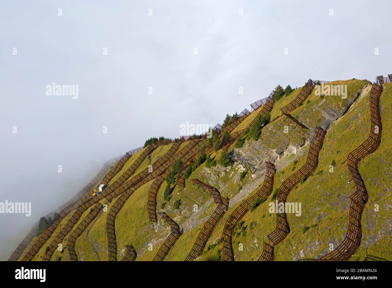 Lawinenbarrieren am Gipfelhang des Maennlichens bei Wengen. Blick auf das unter einer Nebeldecke liegende Lauterbrunnental. Stockfoto