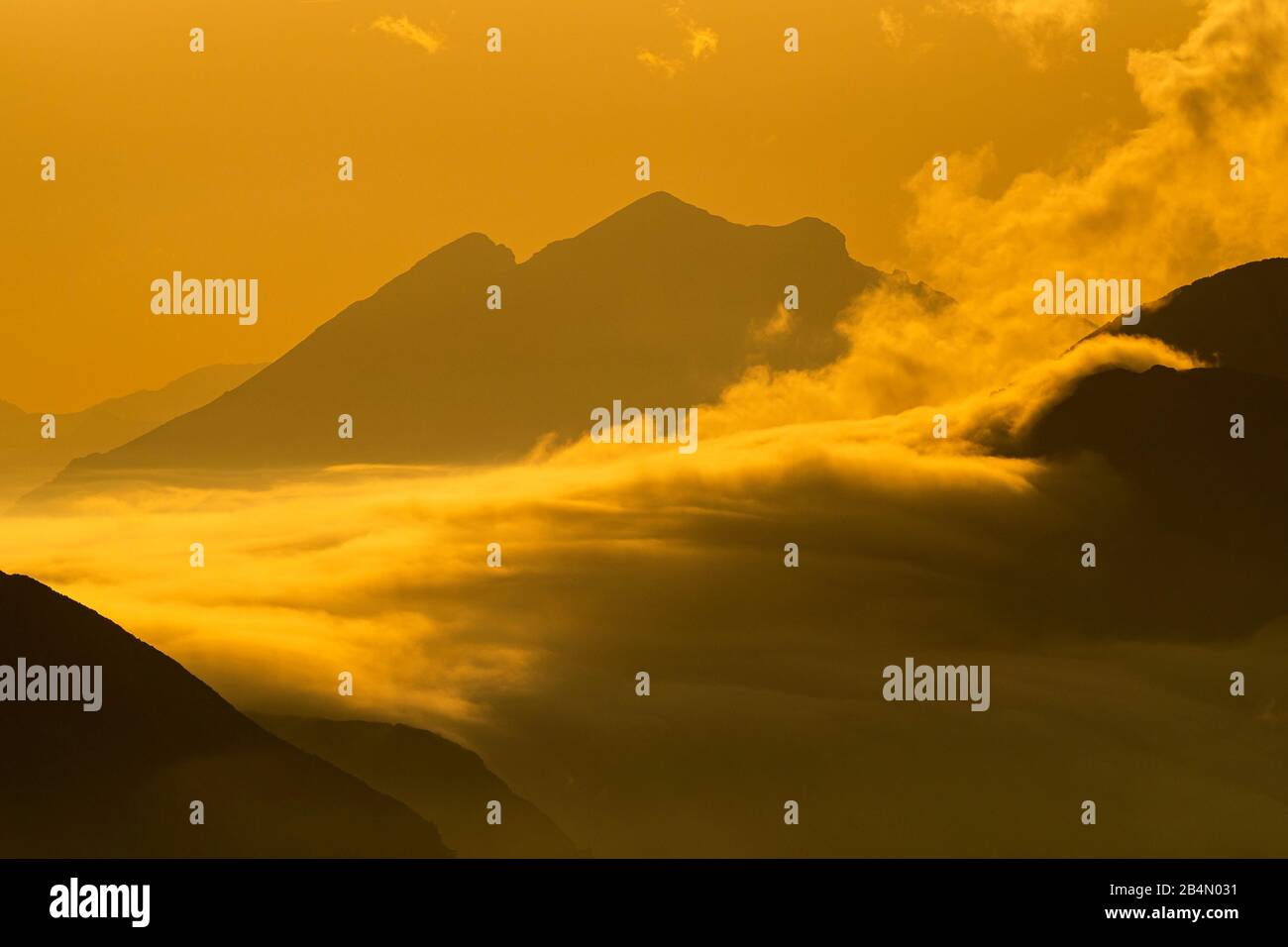 Hoher Nebel schwimmt im goldenen Abendlicht über das Plumsjoch im Karwendel, von den Rofan-Bergen aus gesehen. Stockfoto
