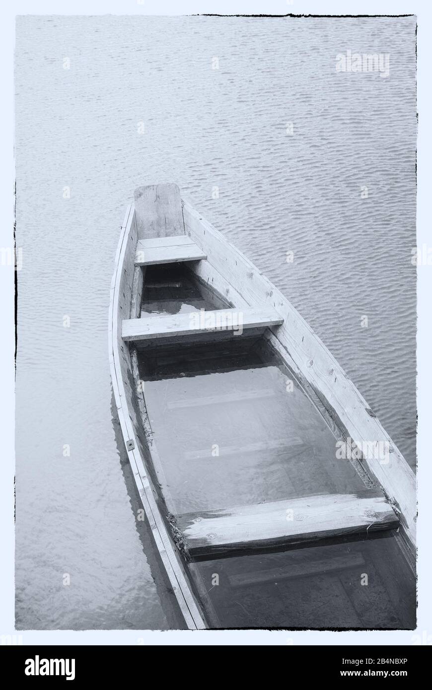 Kunstbild in Schwarzweiß. Ein Holzboot an einem nebligen See. Stockfoto