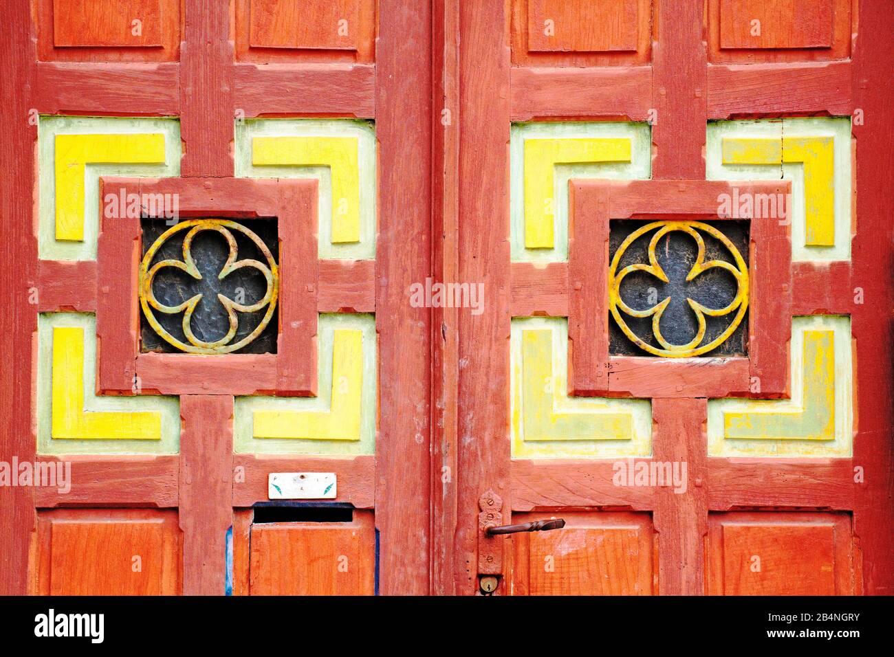 Auffällige rote Holztür mit Kassettenplatten und stilisierter Blume. Tréguier ist eine Gemeinde im Département Côtes-d'Armor in der Bretagne. Tréguier ist die historische Hauptstadt des Trégor. Stockfoto