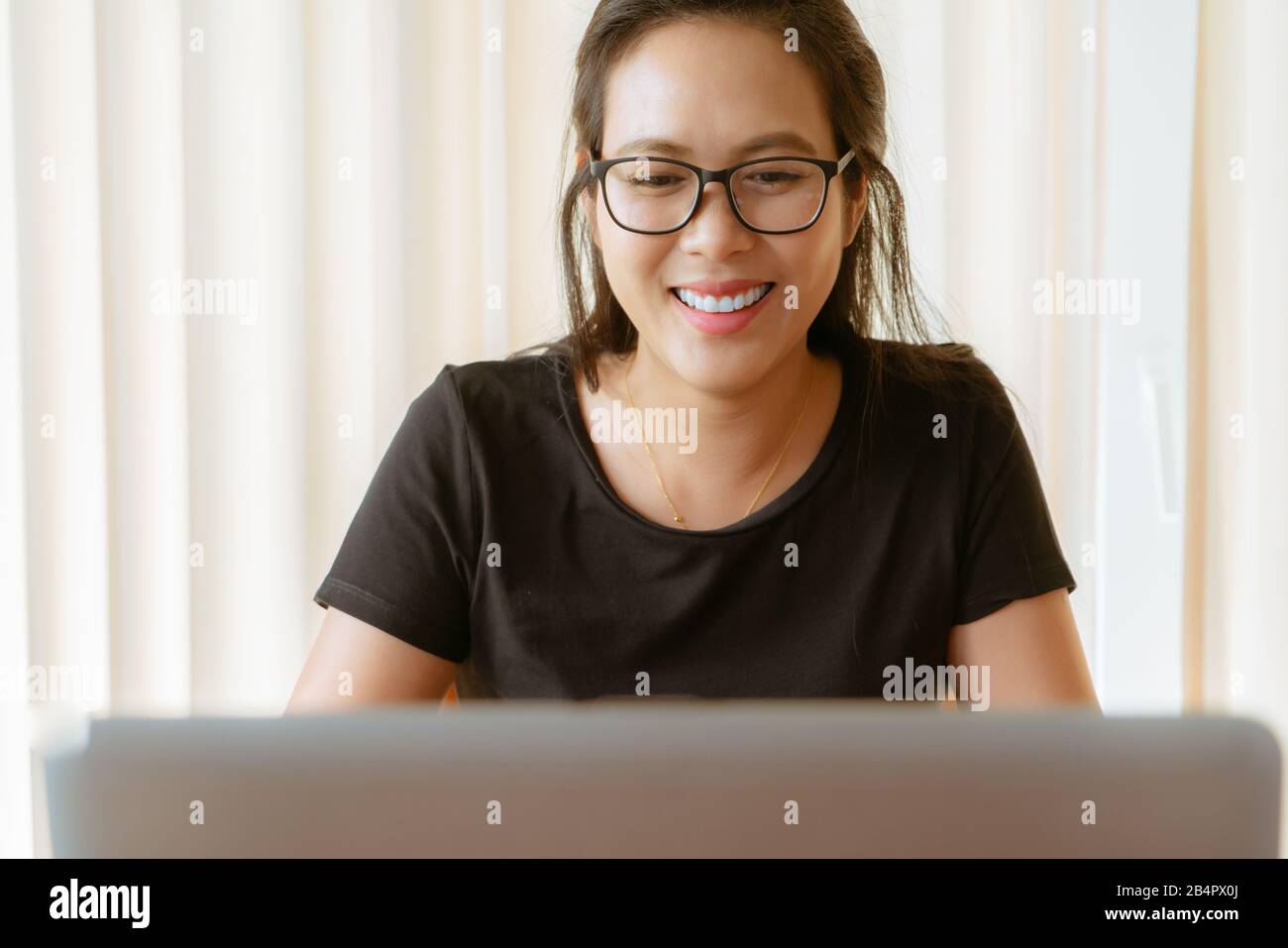 Glückliche Frau mit Laptop. Junge asiatische Frau, die zu Hause sitzt und am Laptop arbeitet Stockfoto