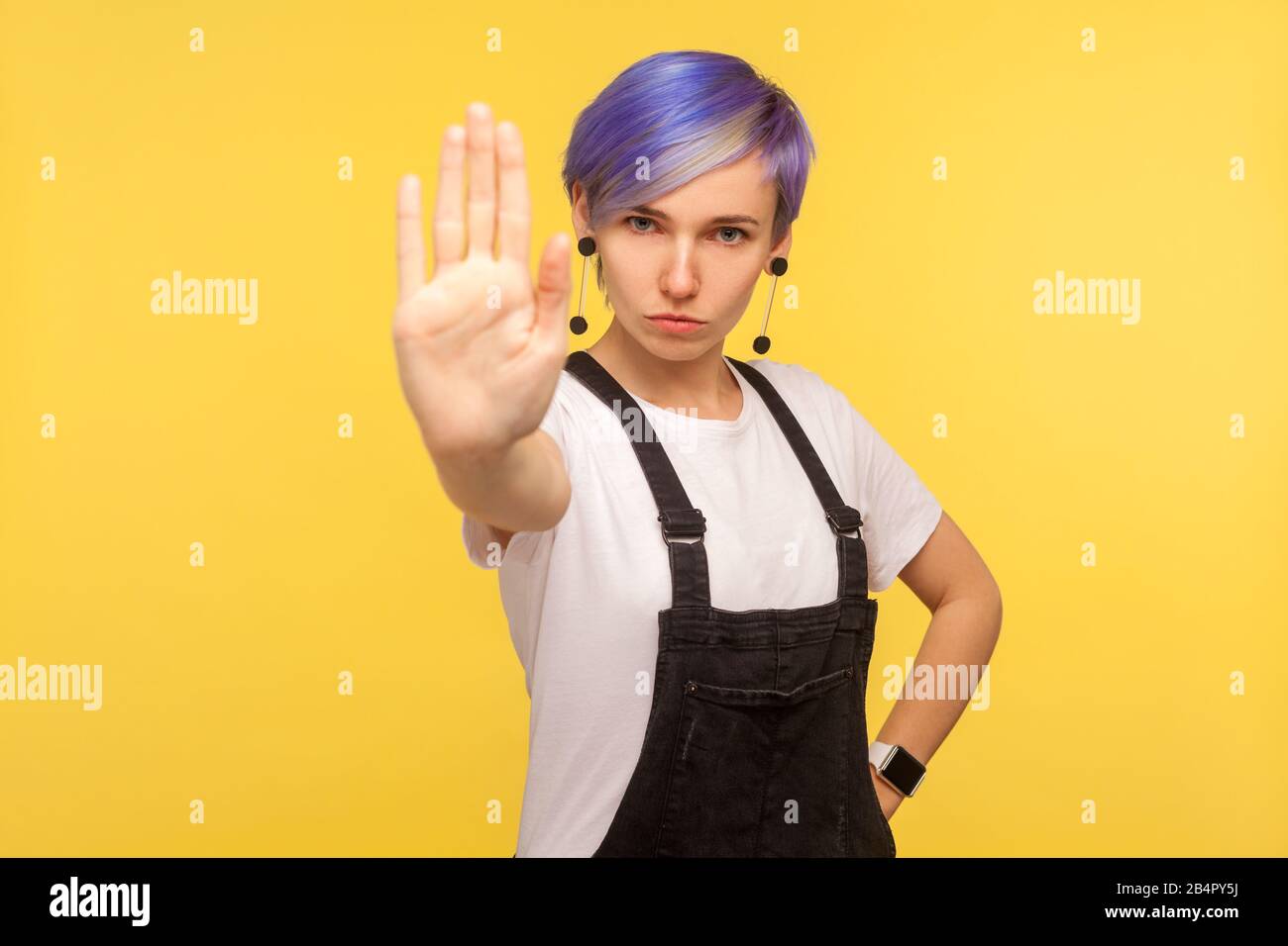 Nein, verboten! Porträt einer ernsthaften Hüftfrau mit violettem, kurzem Haar in Denim-Overalls, die ein Stopp-Geste-Limit-Zeichen zeigen und genug sagen, Warnung vor Stockfoto