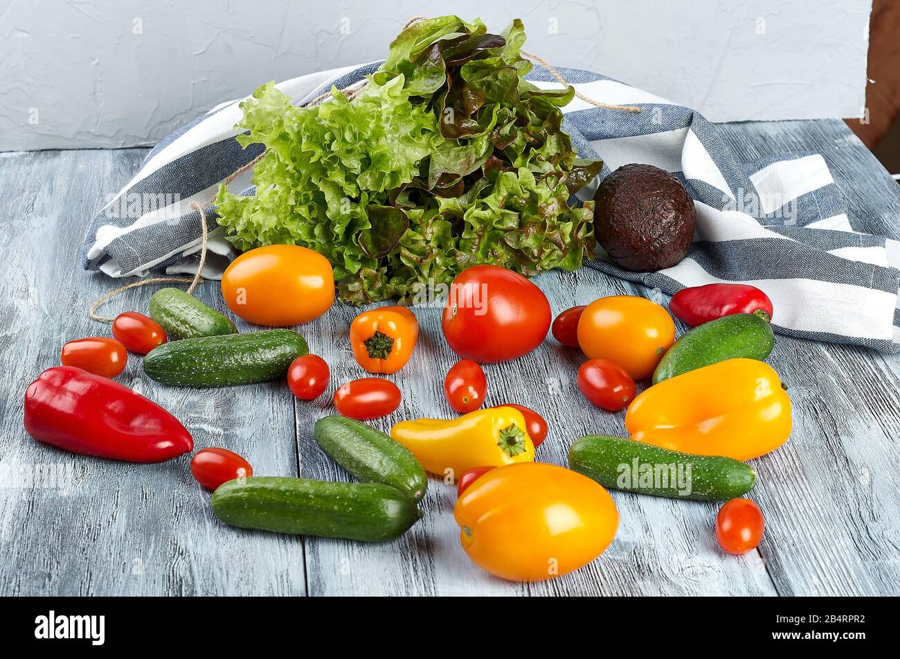 Frisches Mini-Gemüse, Tomaten, Gurken, Paprika, Avocado und Grüns auf grauem Hintergrund. Stockfoto