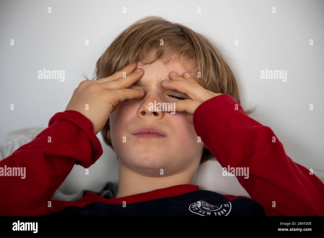 Kind mit Kopfschmerzen, Junge 9 Jahre alt, mit Schmerzen verzerrtes Gesicht, symbolisches Bild, Stockfoto