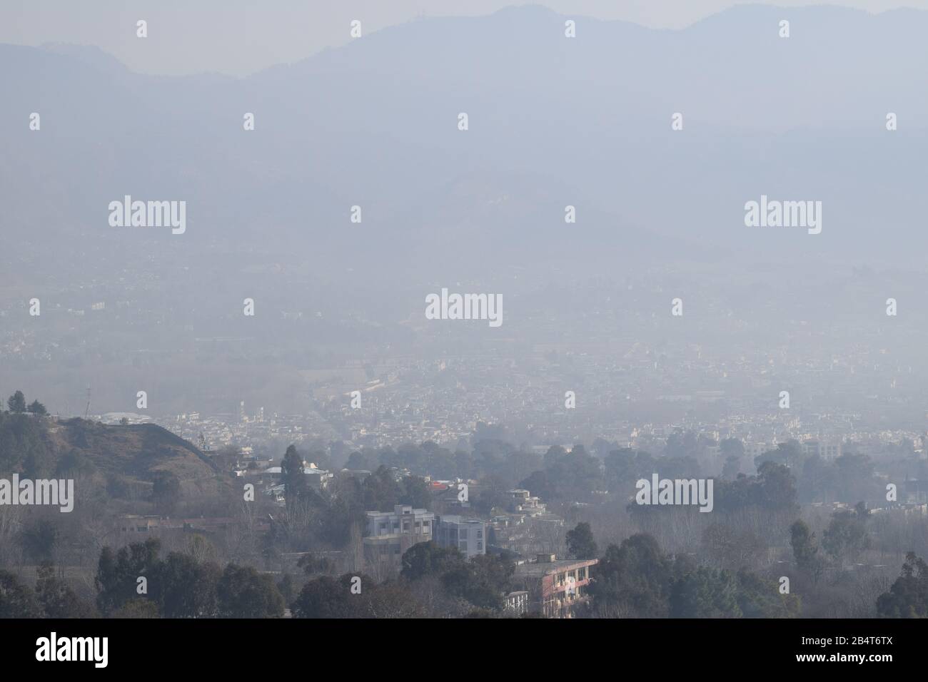 Nebeliger Blick auf die Stadt mit Bäumen, Bergen und Häusern Stockfoto