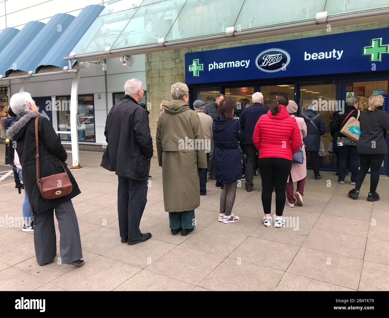 Die Leute warten außerhalb eines Boots Apothekenhauses in West-London, wo die Bestände an Handdesinfektionsmittel auf zwei pro Person begrenzt sind. Stockfoto