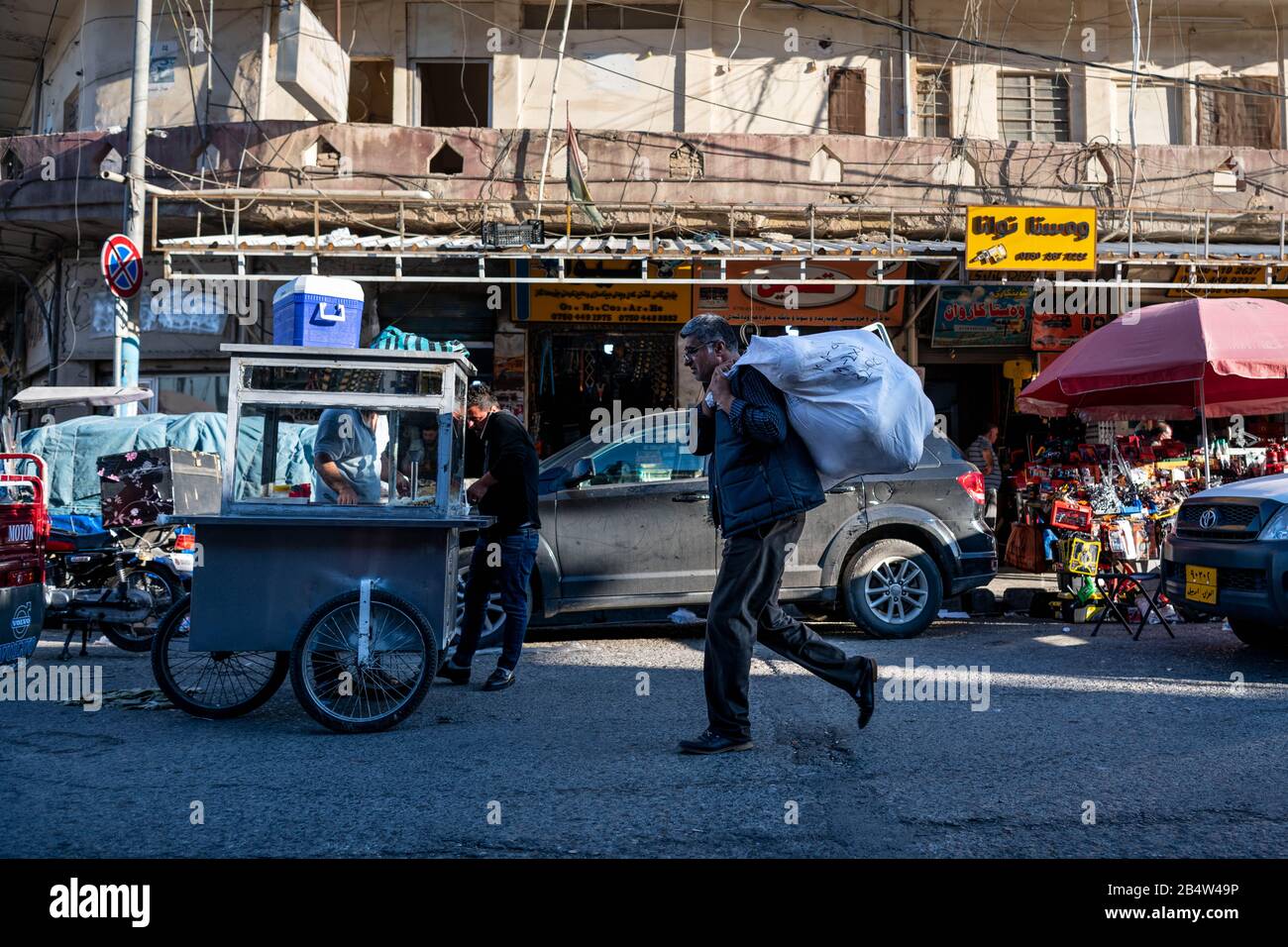 Irak, Iraq Kurdistan, Arbil, Erbil. Im Vordergrund läuft ein Mann mit einem schweren Päckchen auf der Schulter. Stockfoto