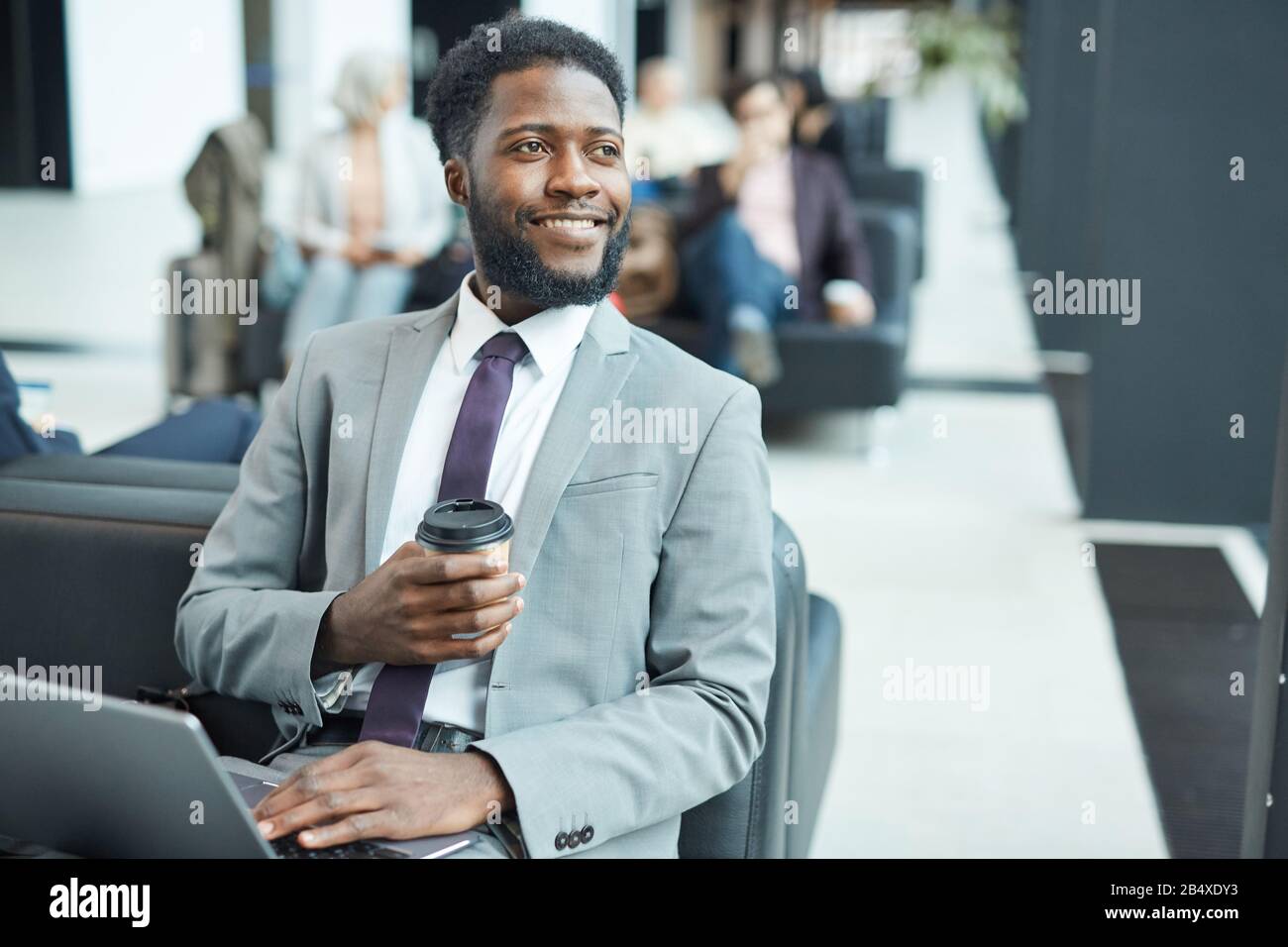 Fröhlicher junger schwarzer Geschäftsmann mit Laptop verbringen Sie Zeit in der Abflughalle und trinken Kaffee, der wegschaut, horizontales mittleres Porträt Stockfoto