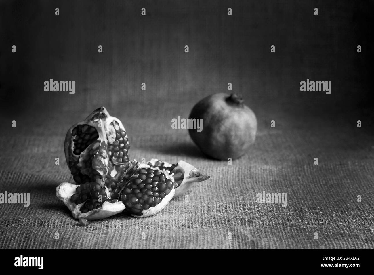 Schwarz-Weiß-Granatapfel und Rohgranaten auf Sacktuchhintergrund. Rustikaler Stil. TTasty Fruit Retro STILL LIFE dunkles Foto Stockfoto