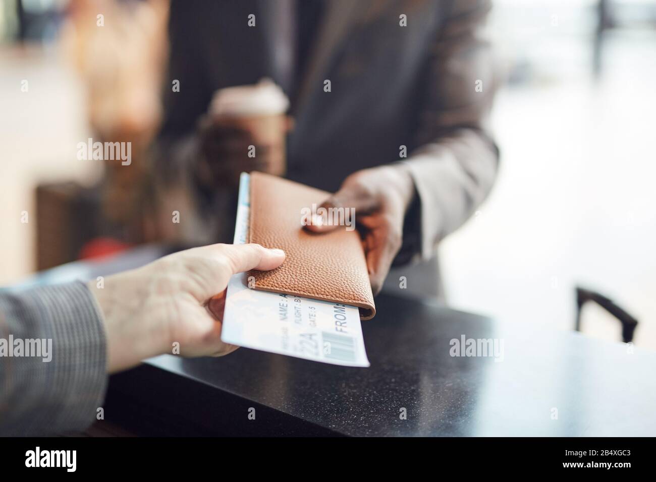 Unerkennbarer Mann, der seinen Pass und sein Flugticket an einen nicht erkennbaren Mitarbeiter des Check-in, einen horizontalen Nahschuss, einen Kopierraum gibt Stockfoto