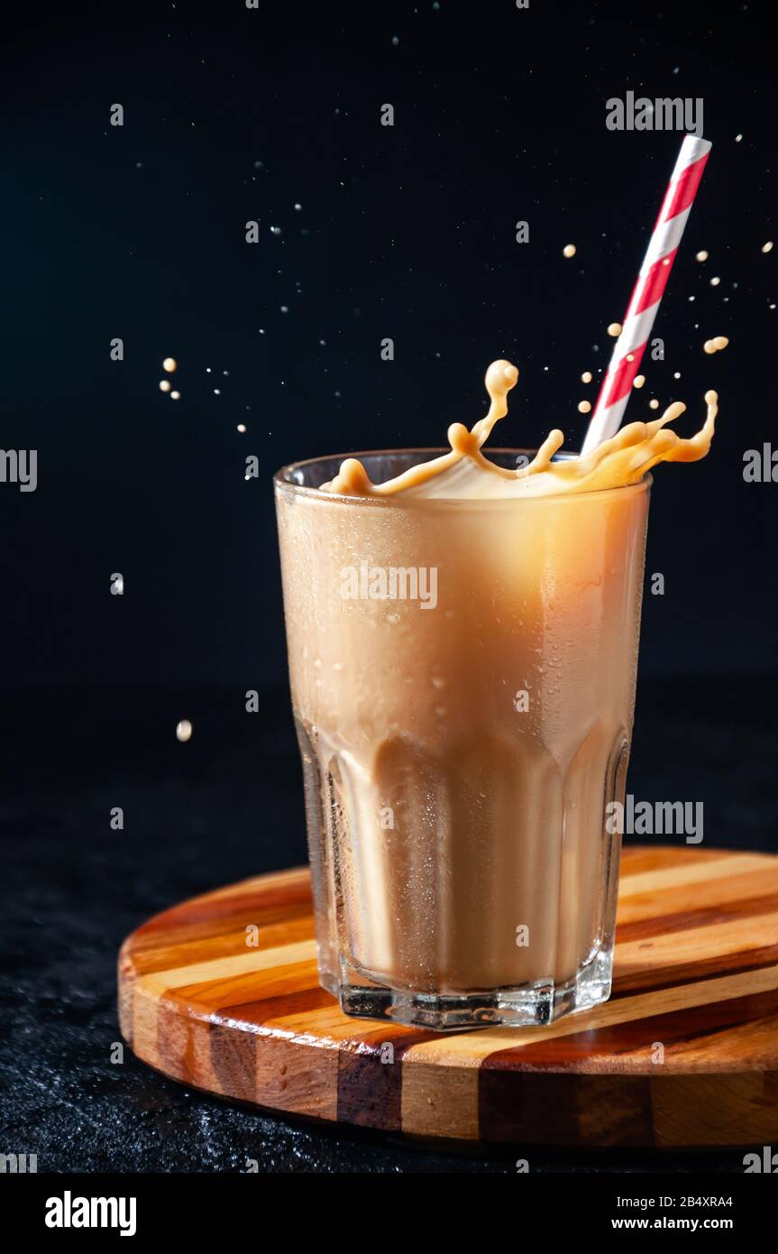 "Splash of Iced Coffee" mit "Straw in Tall Glass" auf dunklem Hintergrund. Konzept Erfrischendes Sommergetränk. Stockfoto