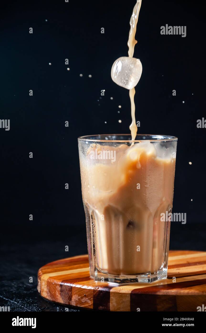 Iced Coffee mit Splash und Ice Cube in Tall Glass auf dunklem Hintergrund. Konzept Erfrischendes Sommergetränk. Stockfoto