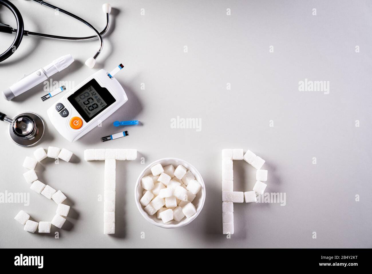 Gesundes Lifestyle-, Lebensmittel- und Sportkonzept. Draufsicht über Diabetes-Testerset und Stethoskop mit Würfeln ZUCKERSTOPPZEICHEN auf dunkelgrauem Hintergrund. Stockfoto