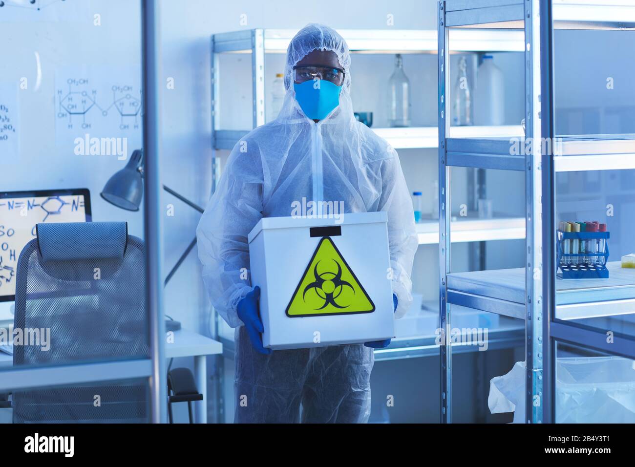 Horizontaler mittlerer, langer Schuss unerkennbarer Labormitarbeiter in einer Schutzhülle für Arbeitskleidung mit biologischen Gefahren Stockfoto