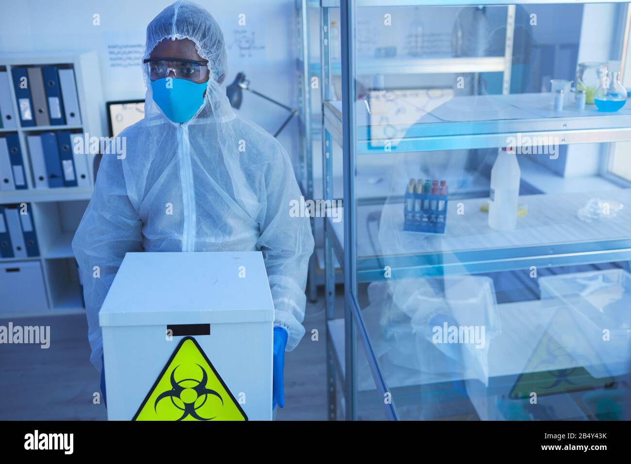 Horizontaler, hochwinkeliger, nicht erkennbarer Labormitarbeiter in einer schützenden Tragebox mit biologischen Gefahren Stockfoto