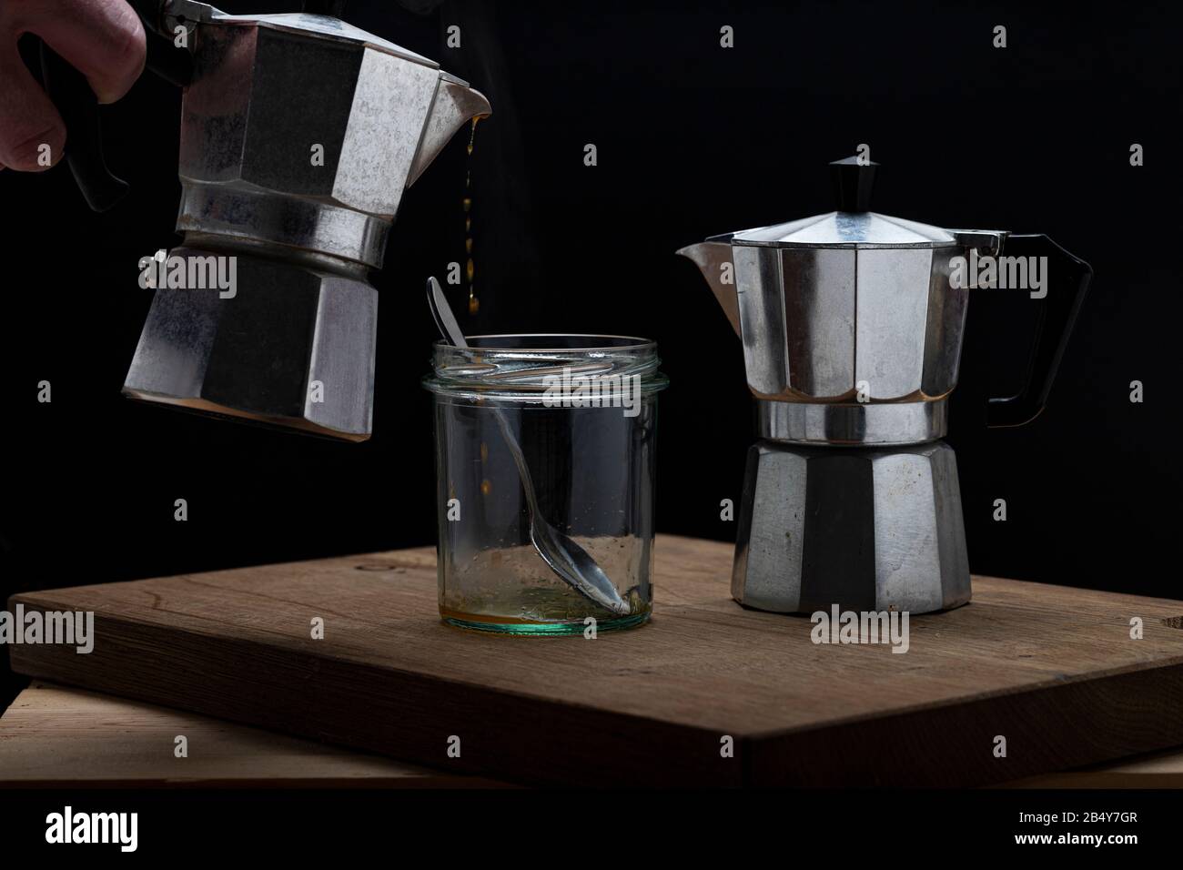 Heißes Dampfgaren erfrischender Kaffee in einem Glas auf dunklem Hintergrund. Gießen von Moka-Hersteller in leeres Glas mit Löffel Stockfoto