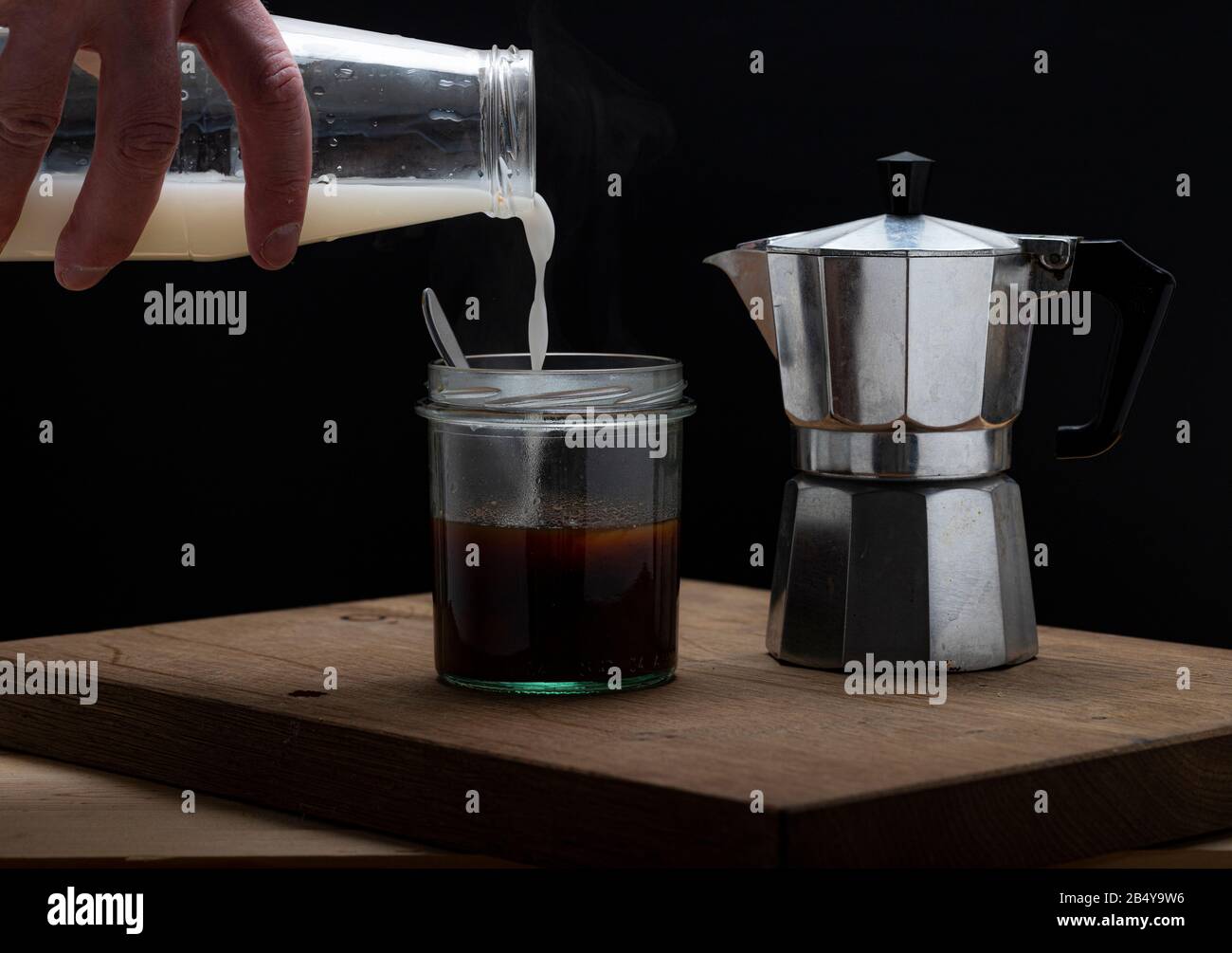 Heißes Dampfgaren erfrischender Kaffee in einem Glas auf dunklem Hintergrund. Gießen von Moka-Hersteller in leeres Glas mit Löffel Stockfoto