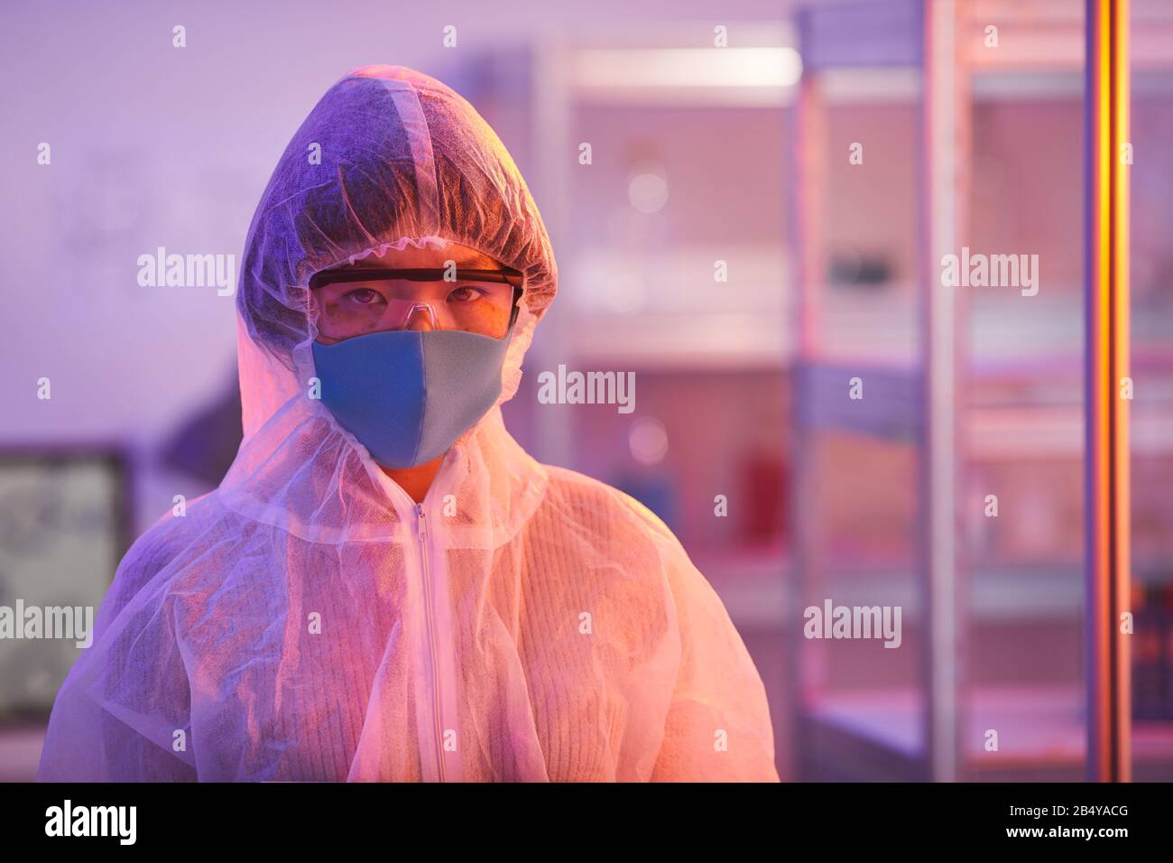 Horizontales Mittel-Nahaufnahme-Porträt von jungen Menschen, die eine schützende Laboruniform tragen, mit Blick auf Kamera, Rosa und gelbes Licht Stockfoto