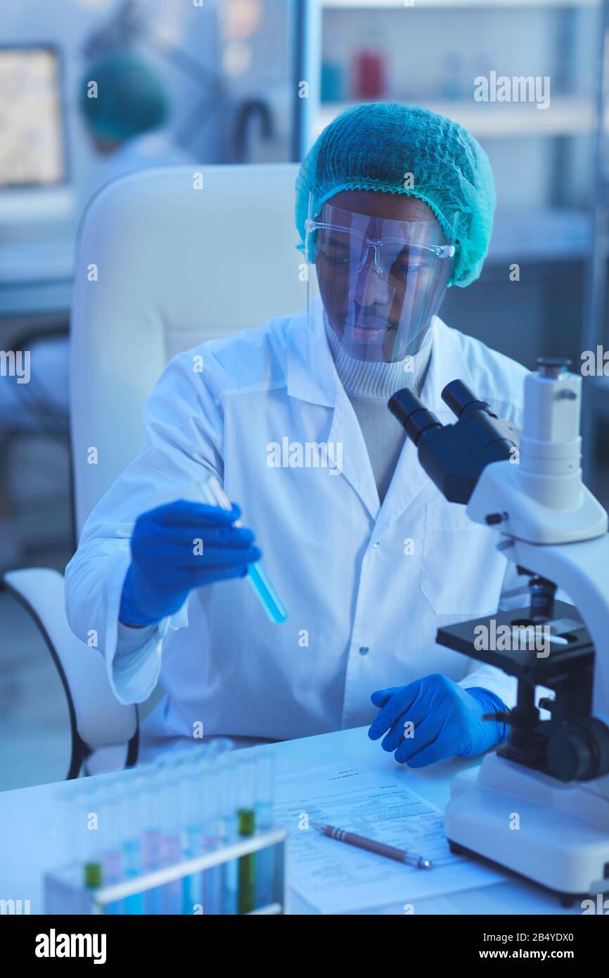 Vertikaler Mittelwinkelschuss von jungen männlichen Medizinwissenschaftlerin, der das Reagenzglas mit blauer Flüssigkeit in Laboruntersuchungen hält Stockfoto