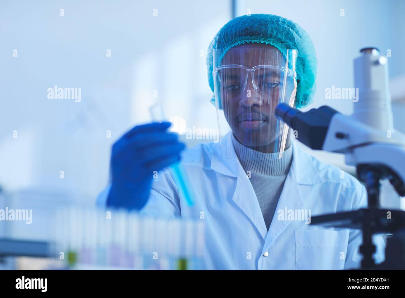 Horizontales Brustbild des jungen männlichen Medizinwissenschaftlers, der eine Schutzmaske trägt, die Labortests durchführt, Kopierraum Stockfoto