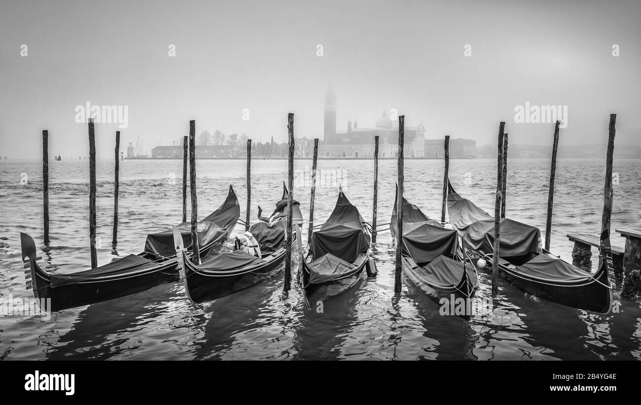 Gondeln in Venedig festgemacht. Italien mit der Insel Saint Giorgio Maggiore im Hintergrund an einem kalten, nebligen Winternachmittag im Dezember Stockfoto