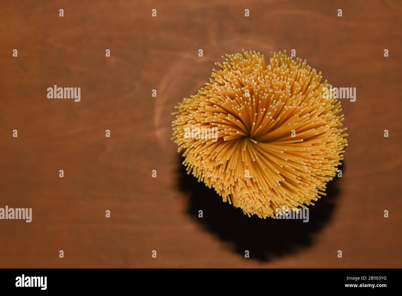 Draufsicht auf gelbe, unbehaarte Spaghetti-Pasta auf einem braunen Holztisch, Aufnahmen mit blitzhartem Licht, Kopierraum für kulinarischen Rezepttext oder Restaurant Stockfoto