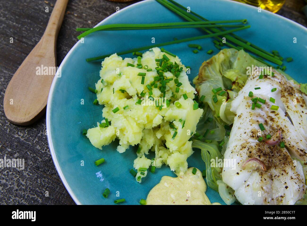 Isoliertes blaues china-gericht mit Codfish-Filet auf Spitzkohl, Senfsoße und Kartoffelpüree, gewürzt mit Schnittlauch Stockfoto