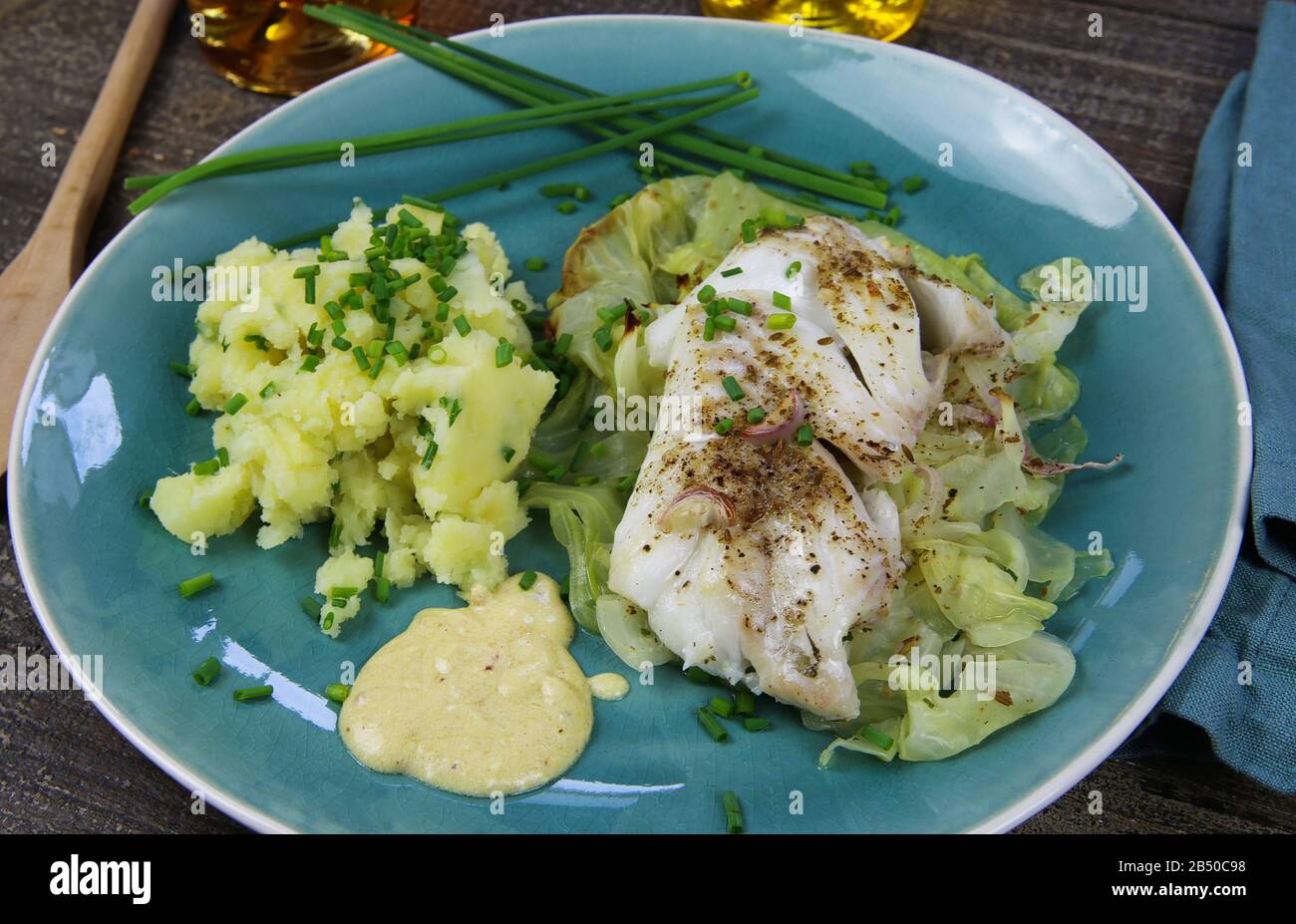 Isoliertes blaues china-gericht mit Codfish-Filet auf Spitzkohl, Senfsoße und Kartoffelpüree, gewürzt mit Schnittlauch Stockfoto