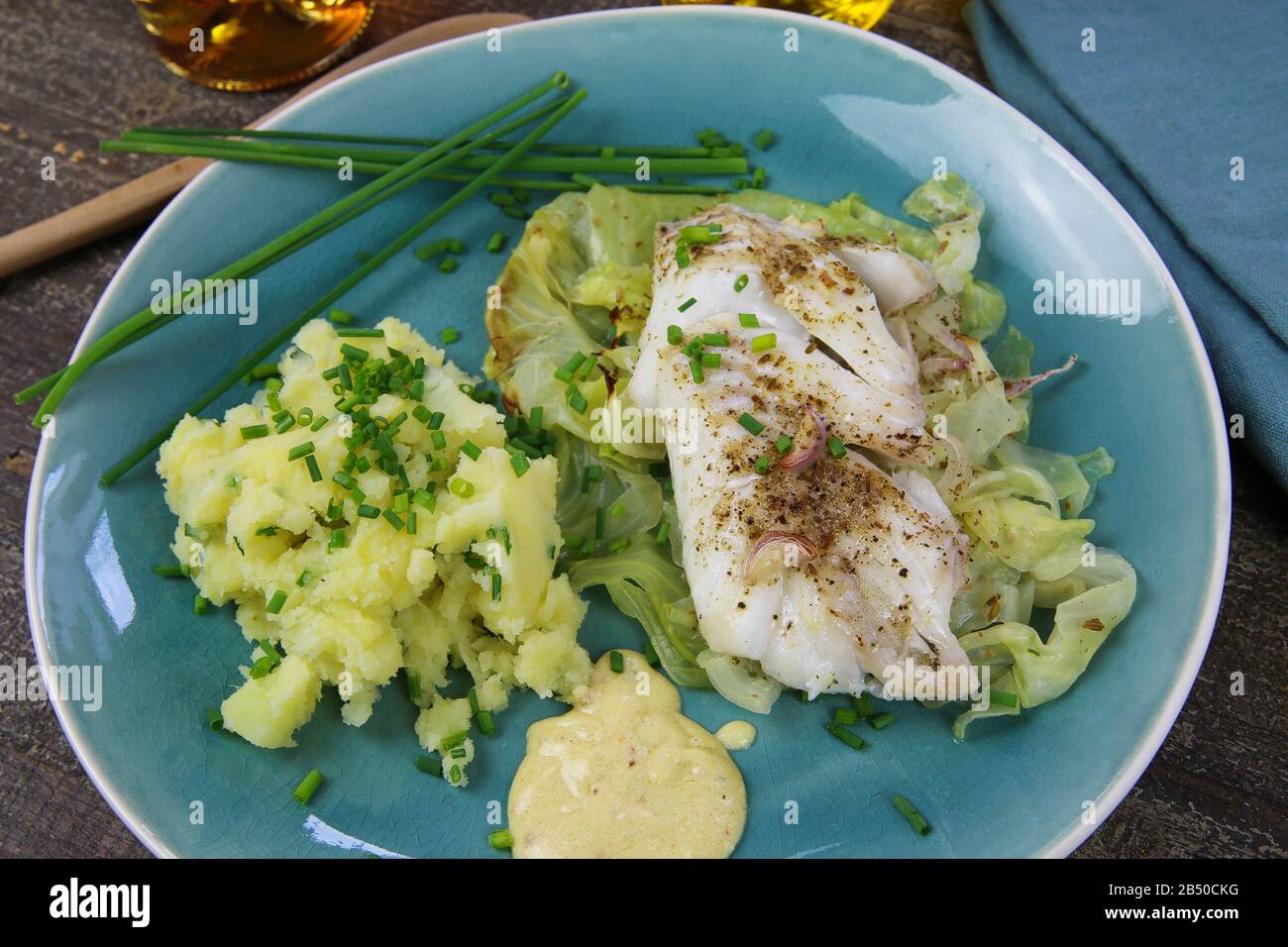 Isoliertes blaues china-gericht mit Codfish-Filet auf Spitzkohl, Senfsoße und Kartoffelpüree, gewürzt mit Schnittlauch Stockfoto