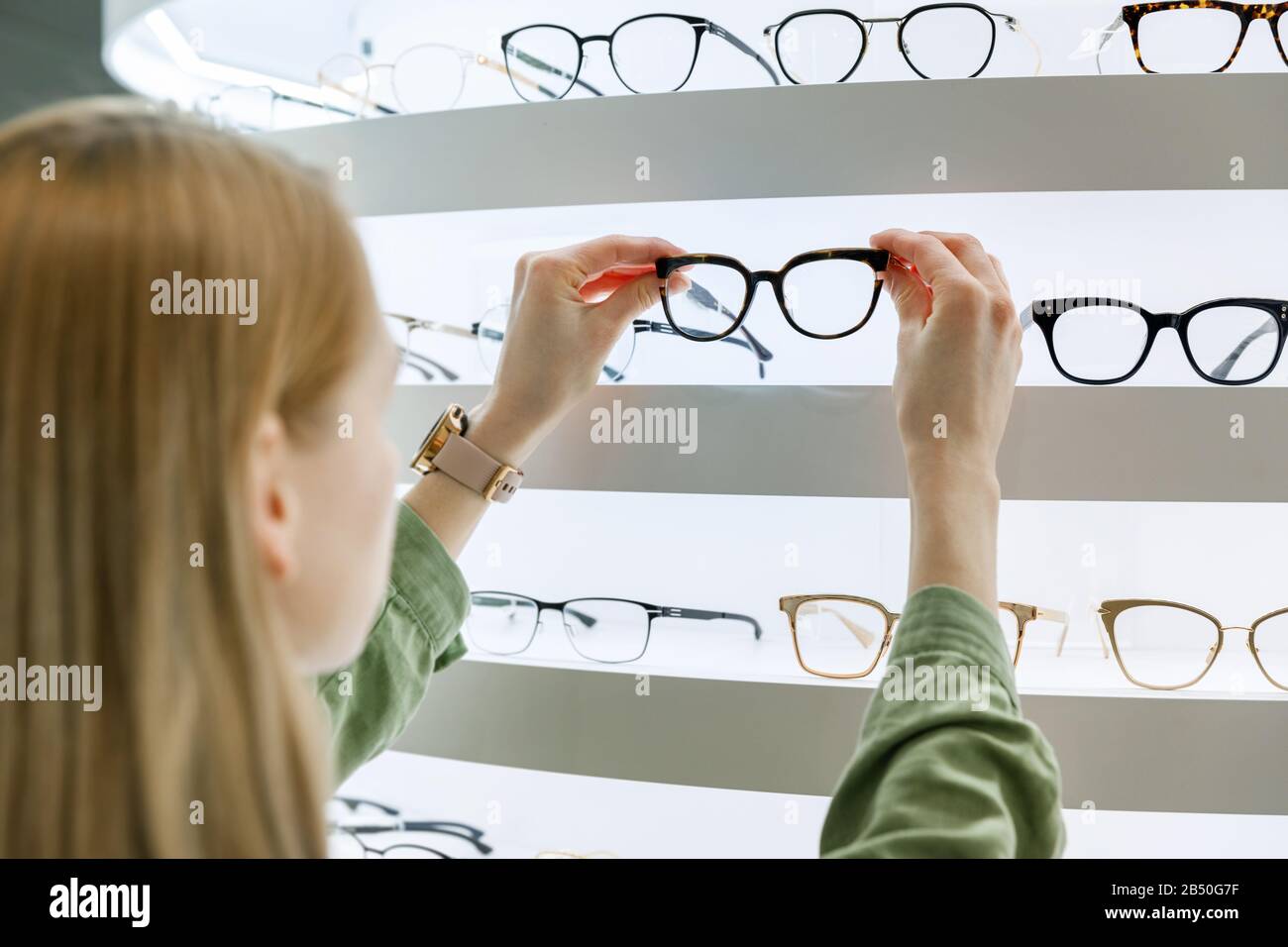 Frau wählt eine Brille aus dem Regal im Optikladen Stockfoto